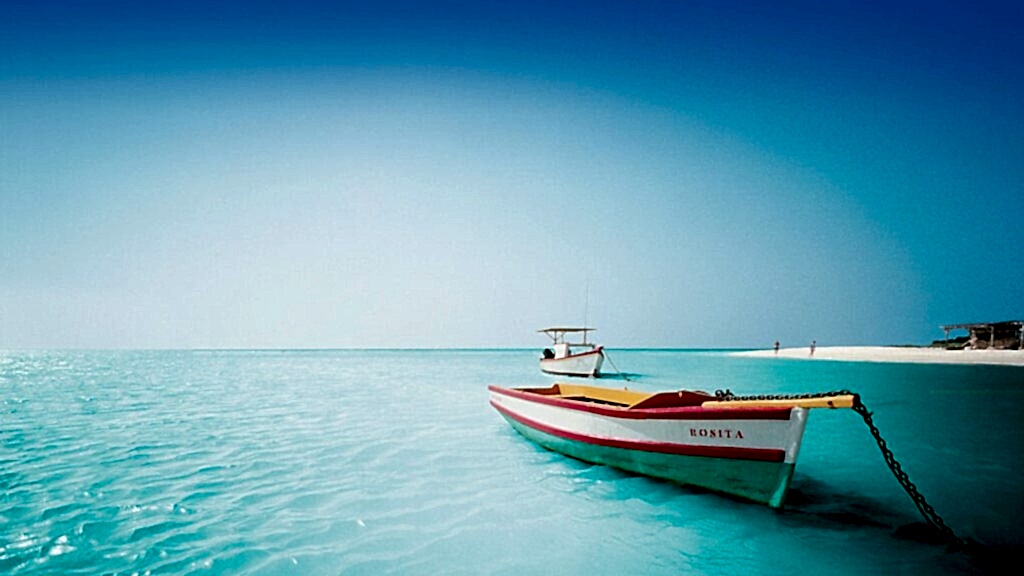 Serene tropical shoreline with clear blue water and a colorful boat in the foreground