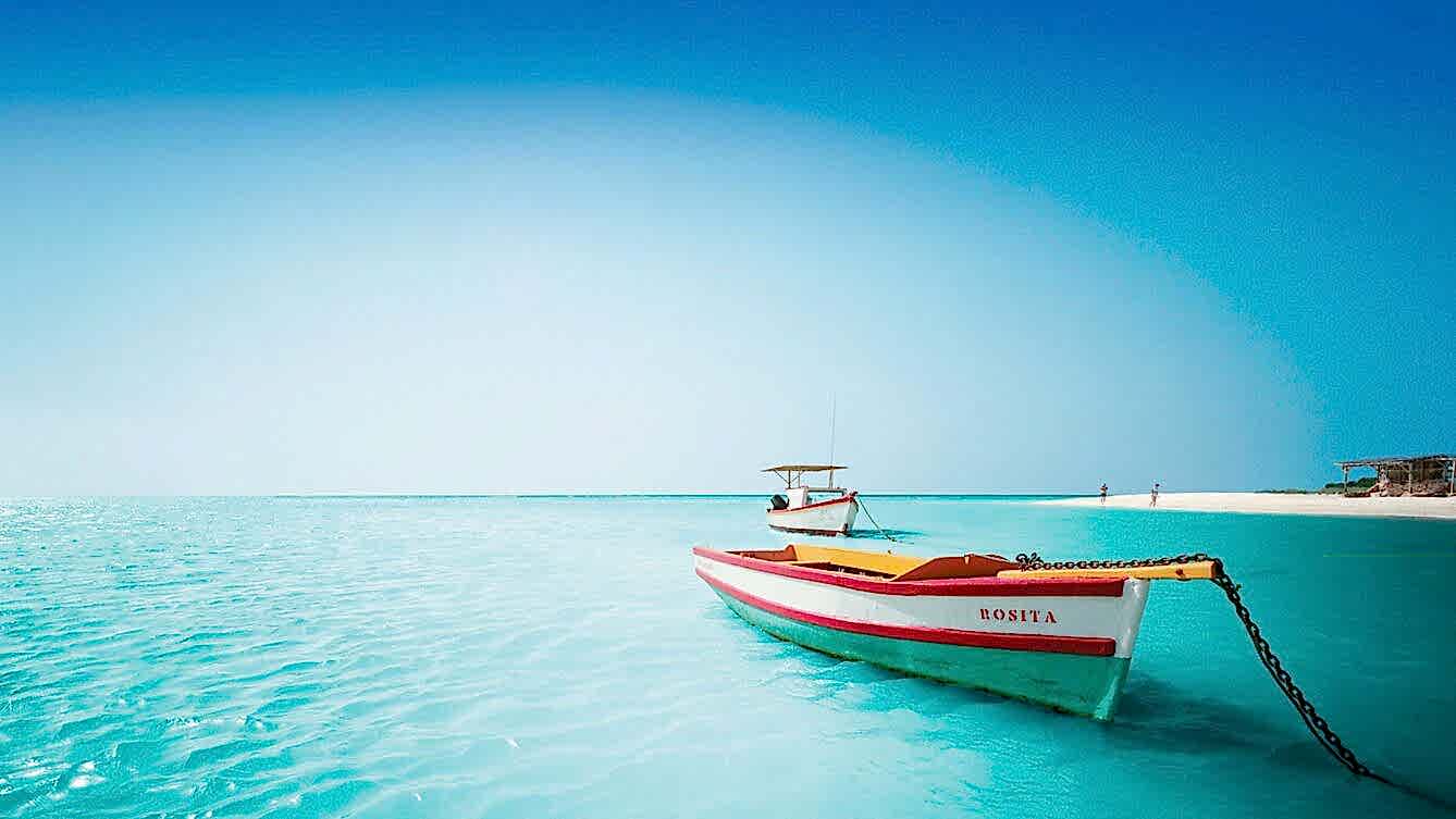 Serene tropical shoreline with clear blue water and a colorful boat in the foreground