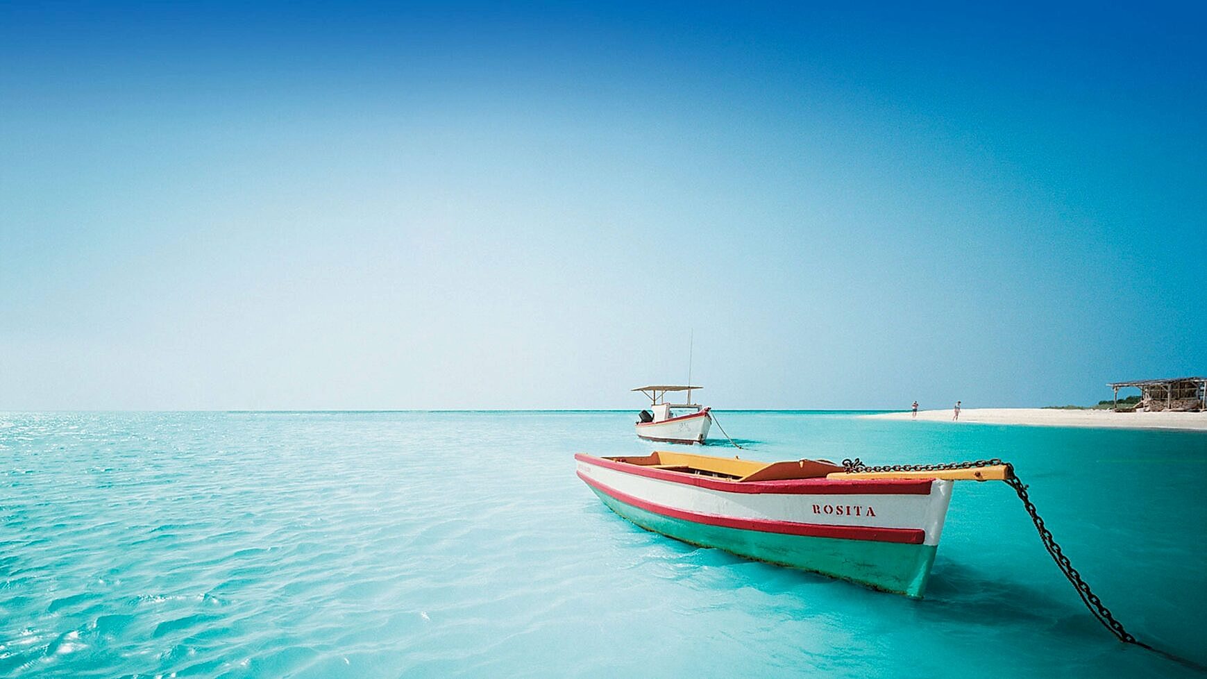 Serene tropical shoreline with clear blue water and a colorful boat in the foreground