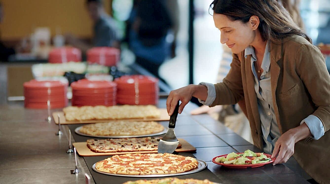 Customer grabbing a slice of pizza with a plate of salad in hand