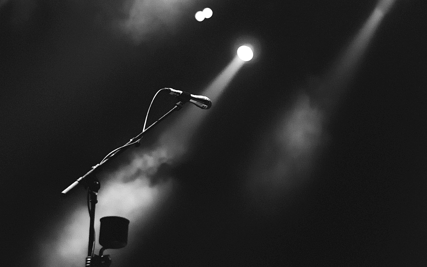 empty stage with a single microphone stand illuminated by a beam of light against a dark background.