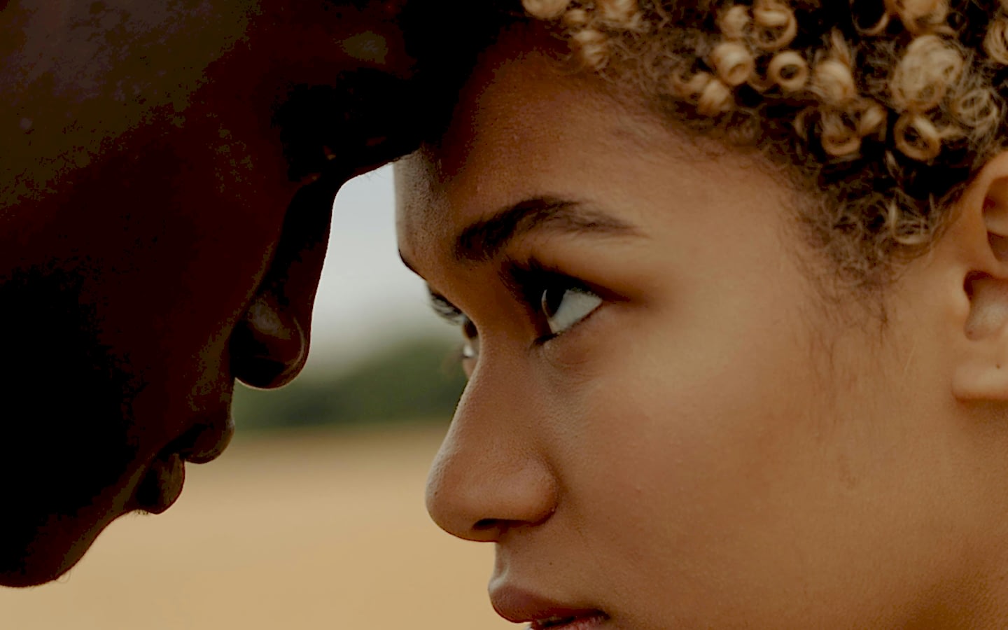 This is a close-up image of a young woman and a man touching foreheads, showcasing an intimate moment. The focus is on the woman's profile, capturing her detailed facial features and expressive eyes set against a blurred natural background.