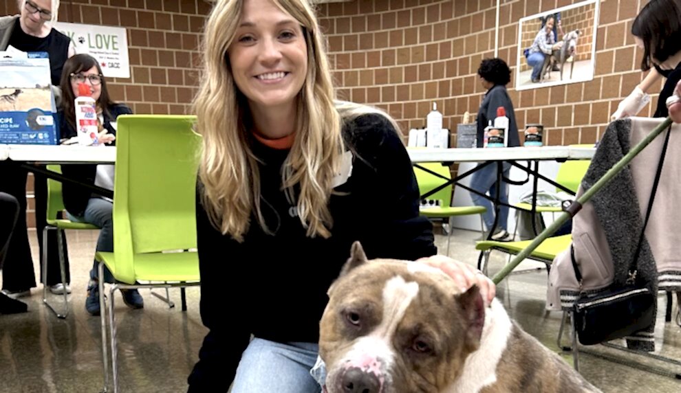 A smiling woman petting a dog at an indoor event.